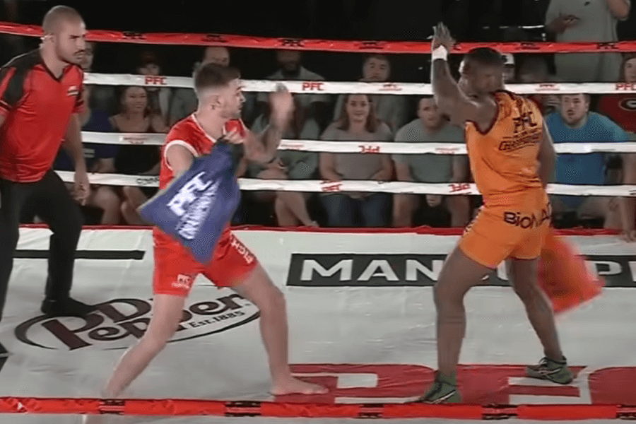 The image shows two contestants in a boxing ring, engaging in a pillow fight as part of a professional or organized pillow fighting competition, with a referee closely observing the match.