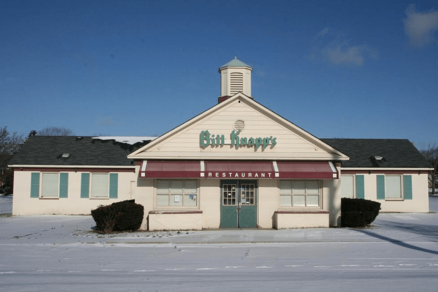 This image shows a closed Bill Knapp's restaurant, a nostalgic building with a white facade, teal accents, and a signature red awning. 