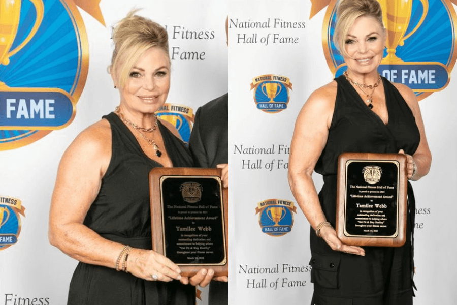 The image shows a woman wearing a black dress, holding a plaque and smiling proudly in front of a backdrop for the National Fitness Hall of Fame, celebrating her lifetime achievement award in fitness.