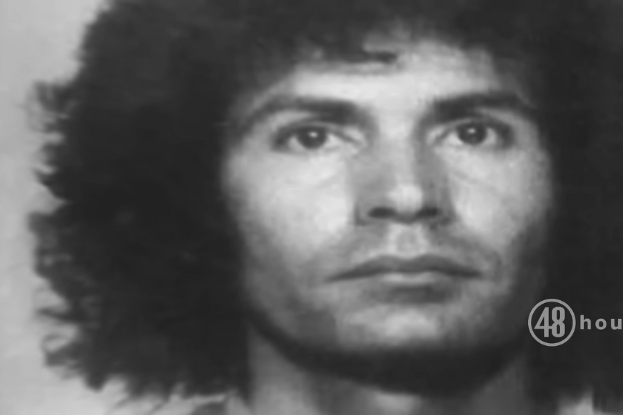 This image appears to be a black-and-white mugshot of Rodney Alcala with curly, voluminous hair, looking directly at the camera with a serious expression. 