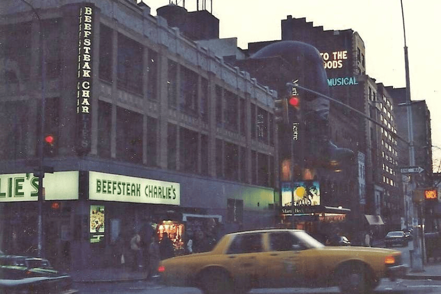 This image captures a nostalgic city scene featuring Beefsteak Charlie's, a classic restaurant with its bright, glowing sign, set in a bustling urban environment with a yellow taxi passing by under evening lights.