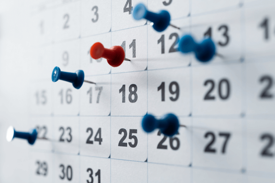 This image shows a close-up of a calendar with push pins marking specific dates. The pins are in various colors, with one prominent red pin placed on the 11th and several blue pins scattered across other dates. The focus on the pins suggests these dates might hold significance, perhaps for marking events, deadlines, or reminders.