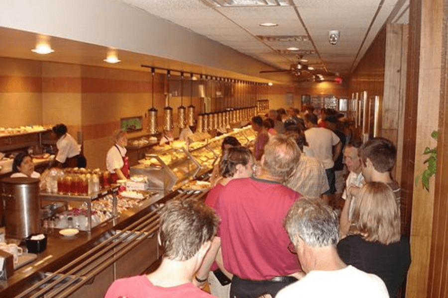 This image captures a busy cafeteria-style restaurant, with customers lining up for freshly prepared food served by employees behind the counter, evoking memories of a warm, communal dining experience.