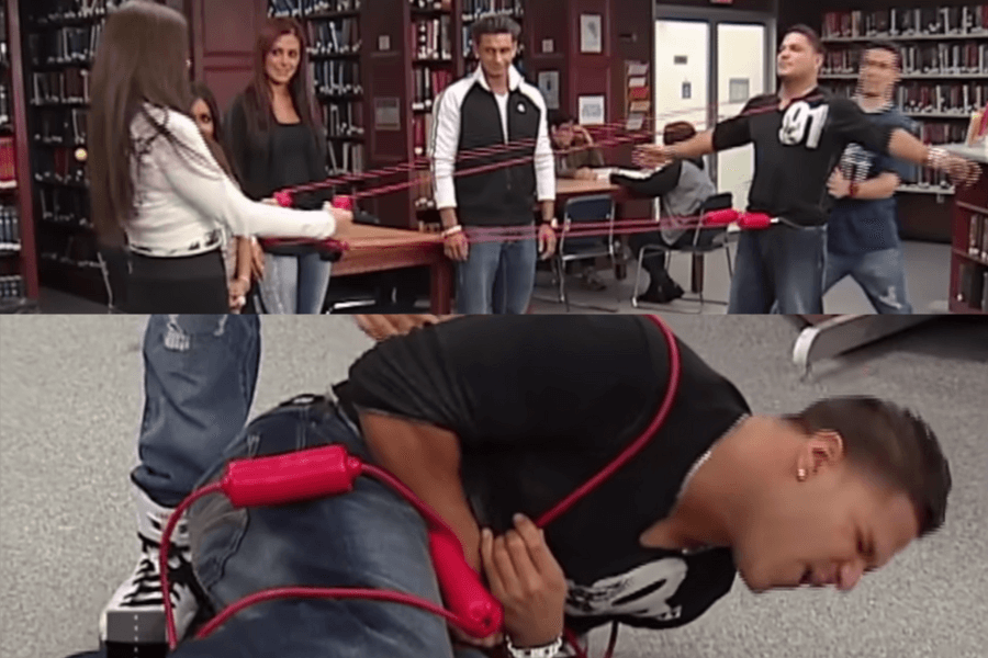 The image shows contestants in a library setting participating in a game where they endure rubber band slingshot challenges. They appear to be in pain as they’re hit by rubber bands, trying to stay silent despite the discomfort—a classic setup for the Japanese game show Silent Library, where contestants endure bizarre punishments while attempting not to make noise.