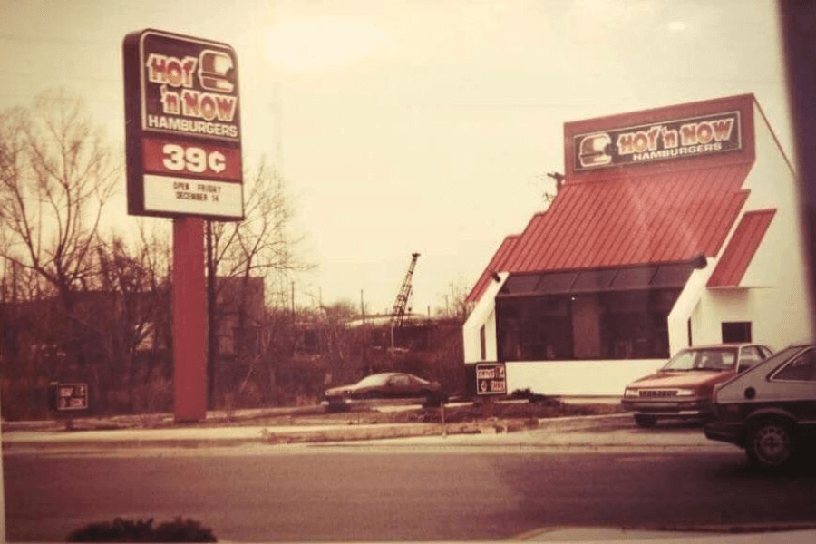 This photo showcases a Hot 'n Now Hamburgers location with its distinct red-roofed architecture and signage advertising 39-cent hamburgers, capturing the essence of a retro fast-food era.