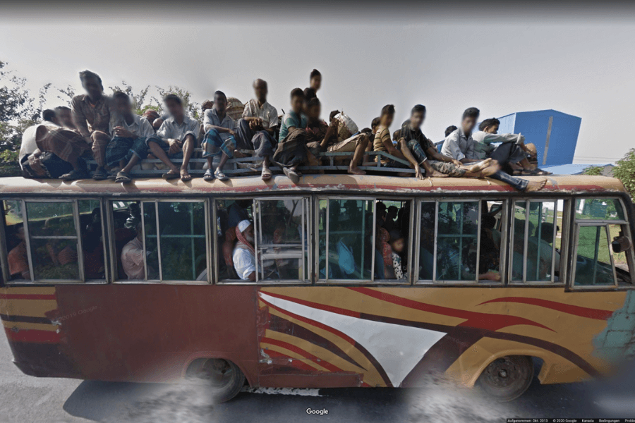 This image shows an overcrowded bus with people sitting on the roof as well as filling the interior. The bus appears to be heavily loaded, with passengers seated on top in close quarters, holding onto their belongings. This scene highlights a common practice in some regions where public transportation is limited or in high demand, leading people to find any available space on the vehicle to reach their destination. The bus itself looks worn, with visible dents and faded paint.