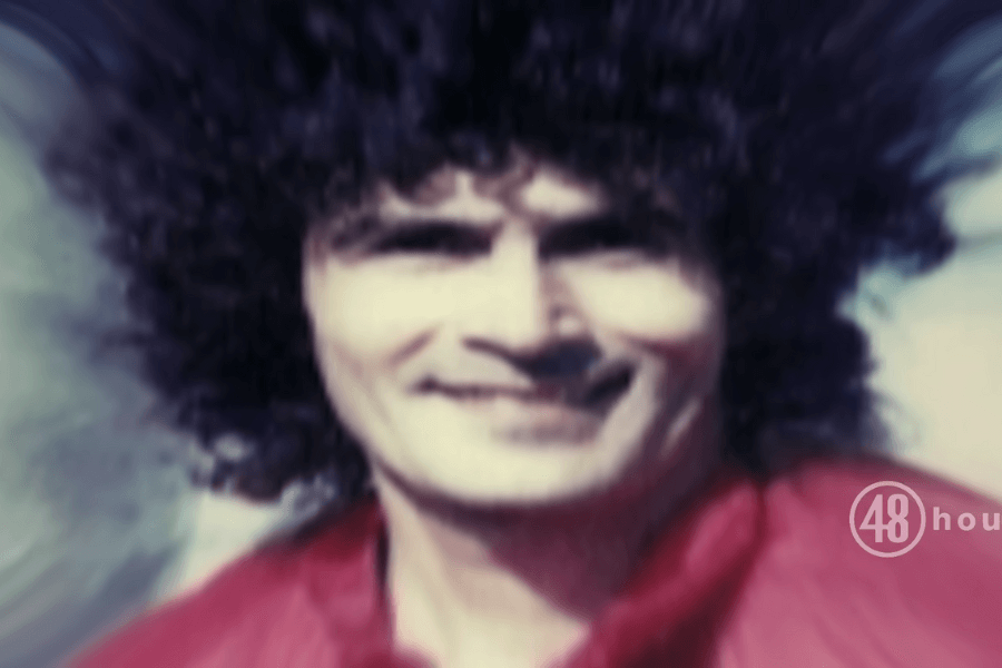 This image displays a blurred photograph of Rodney Alcala with a large, curly hairstyle, wearing a red outfit. The background appears to have been altered or distorted, creating a dynamic, almost swirling effect around the man's head, drawing focus to his face.