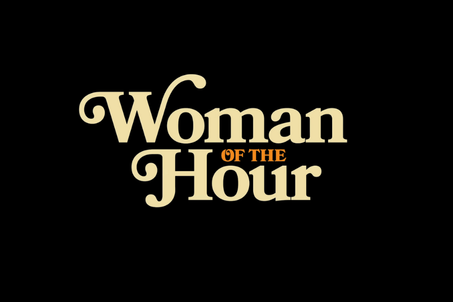 This image displays the title "Woman of the Hour" in a bold, vintage-style font on a black background. The text is primarily a light, cream color, with the words "OF THE" in smaller, orange font between "Woman" and "Hour." The design style suggests a retro or period-inspired theme, with the contrast between cream and orange drawing attention to the central phrase.