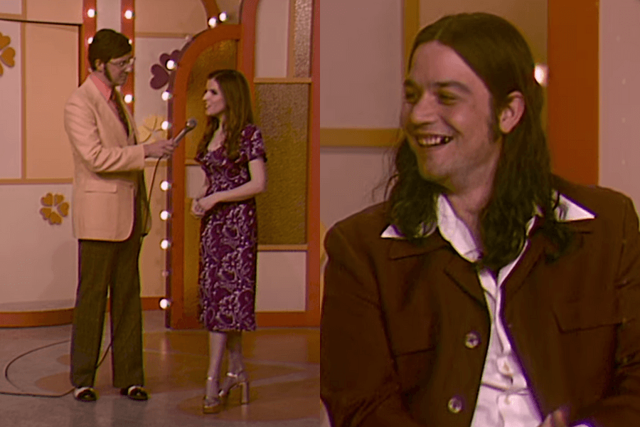 This image shows a recreated scene from The Dating Game in Woman of the Hour, with Anna Kendrick as the contestant being interviewed by the host on the left, and a man portraying Rodney Alcala, smiling on the right.