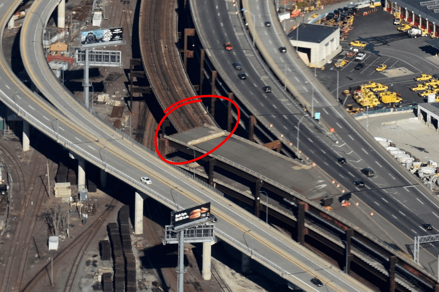 This image shows an aerial view of a highway interchange with multiple elevated roadways. A section of one ramp, highlighted with a red circle, appears to end abruptly, creating a drop-off with no continuation. This incomplete or abandoned ramp contrasts with the surrounding active roads, emphasizing an unusual and potentially hazardous feature within an otherwise functional infrastructure.