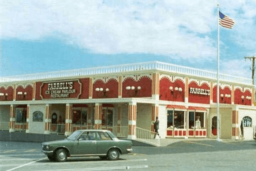 The image shows Farrell’s Ice Cream Parlour Restaurant, a vibrant building with Victorian-style architecture and bright red accents, featuring an American flag nearby, evoking nostalgia for its lively, family-friendly atmosphere and signature ice cream treats.