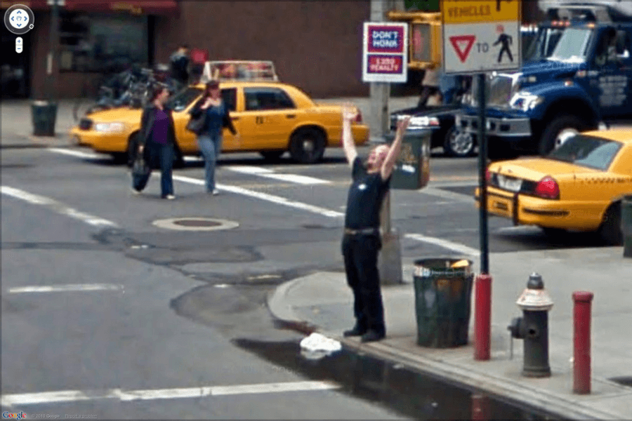 A man stands on a city street corner with his arms raised in celebration, surrounded by taxis and pedestrians, capturing a moment of joyful spontaneity in an urban setting.