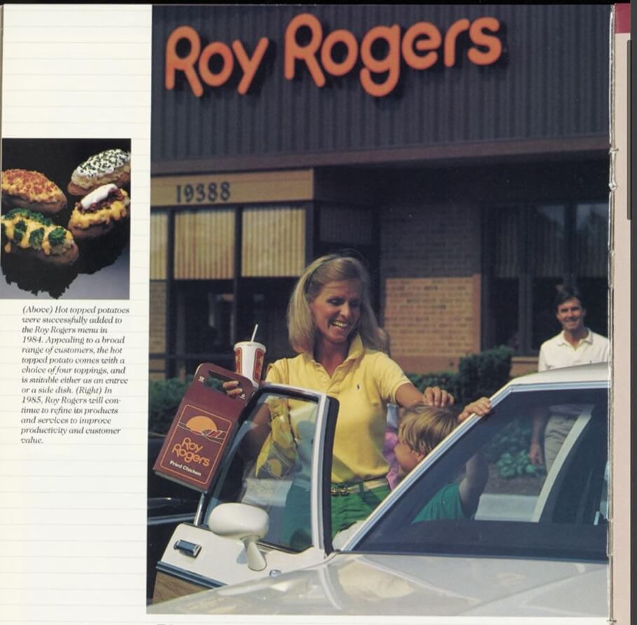 A vintage Roy Rogers restaurant with a brown brick exterior and bold orange signage above the entrance. In the foreground, a smiling woman in a yellow polo shirt holds a Roy Rogers takeout bag and drink while helping a young child into a white car. A man in the background walks toward the scene, and an inset image on the left displays hot topped potatoes, a menu item introduced in 1984.