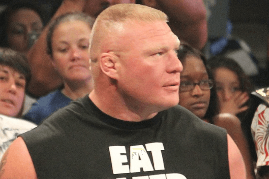 This image depicts a person with a short-cropped hairstyle wearing a sleeveless black shirt with bold white text that starts with "EAT." They are in a crowded indoor setting with onlookers in the background, suggesting a public event or sporting occasion.