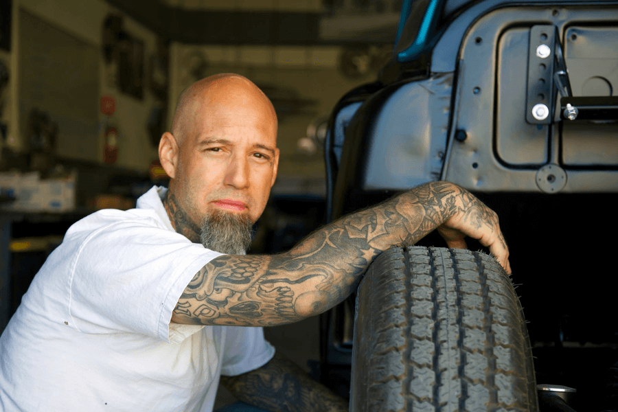 photo of a man arm covered with tattoos sitting beside his truck