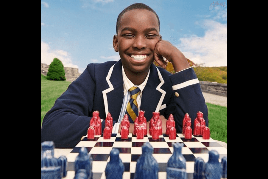 portrait of a kid smiling while a chess board and pieces are in front of him