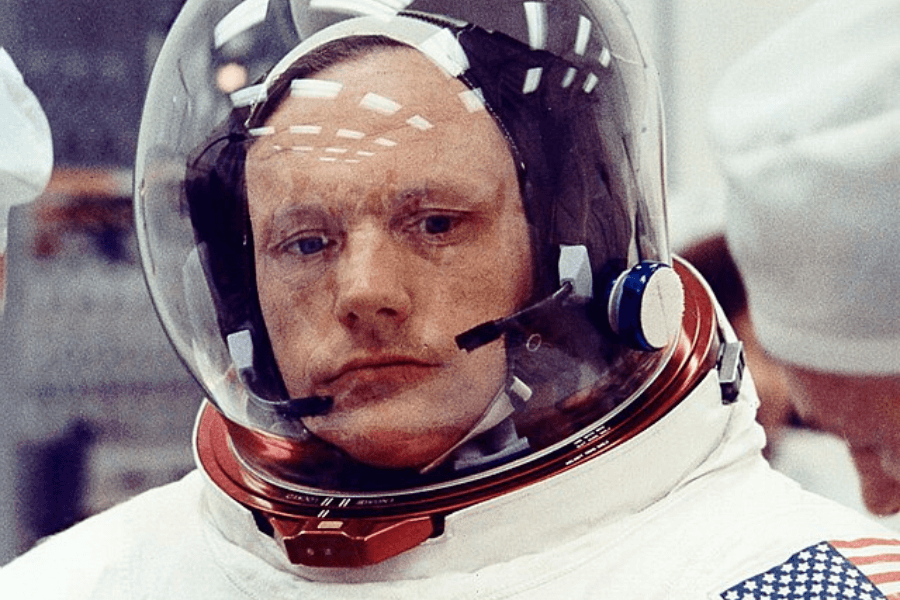 This image shows an astronaut wearing a space helmet and suit, with a reflective visor and a focused expression, preparing for a mission. The American flag patch is visible on the suit’s sleeve, emphasizing a NASA connection or a U.S. space mission.