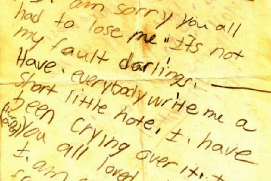 A close-up image of a handwritten note on aged, yellowed paper, with emotional phrases like "I am sorry you all had to lose me" and "it's not my fault, darlings." The informal handwriting and content convey a deeply personal and poignant message, likely written in a moment of vulnerability. The creases and wear on the paper add a sense of history and intimacy to the note.