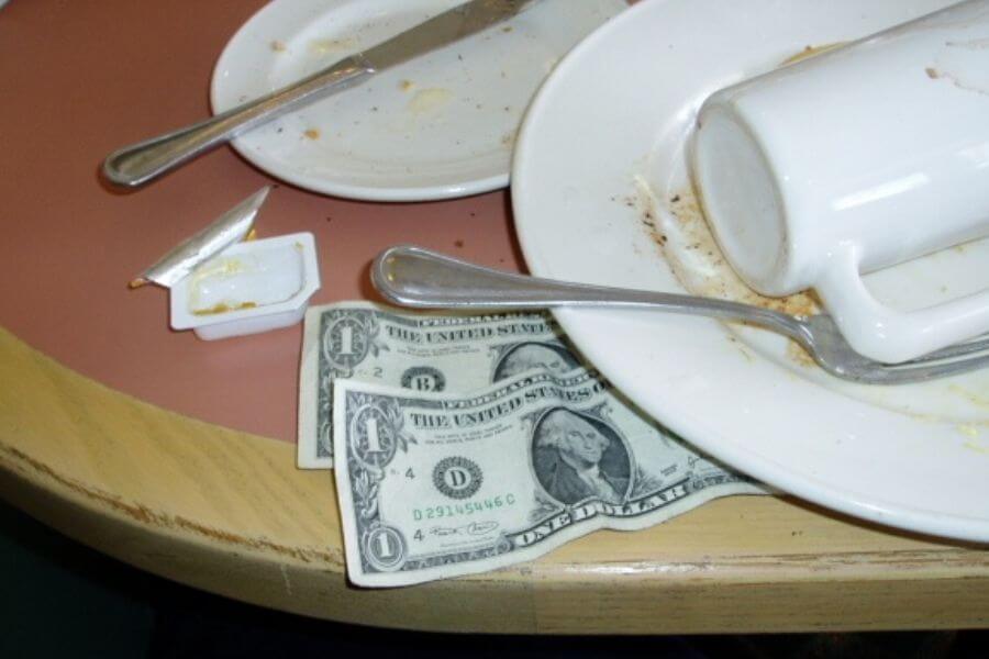 two dollar bills on table next to dirty plates 