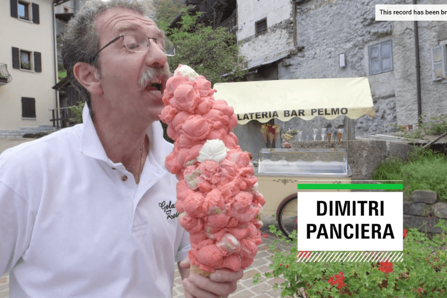 The image features Dimitri Panciera holding and licking an enormous ice cream cone stacked with dozens of scoops of bright pink and white gelato. He is outdoors, with an old-fashioned gelato cart and rustic European architecture in the background. A text overlay with his name emphasizes his likely involvement in a record-setting event related to the oversized gelato creation.