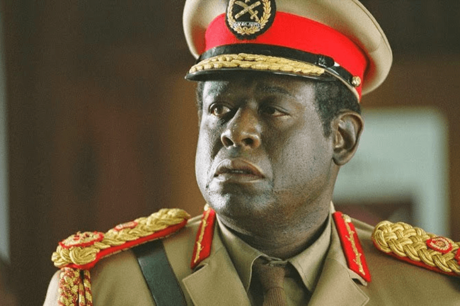 This image depicts a man in a military uniform adorned with gold braiding, red accents, and a peaked cap with insignia. His expression is serious, suggesting a portrayal of authority or leadership in a formal or historical context.