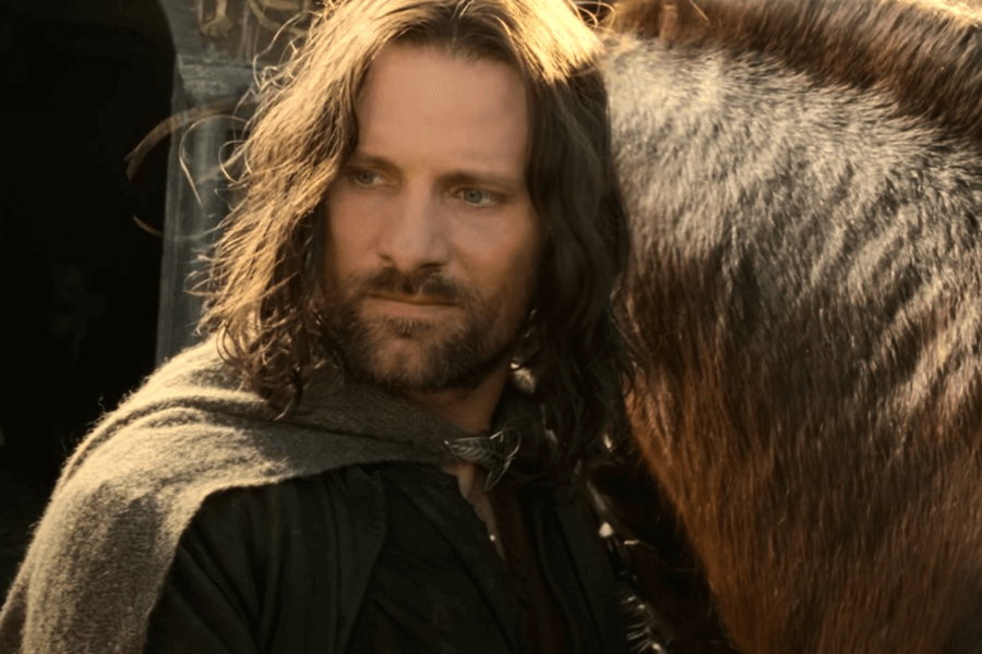 This image features a man with shoulder-length hair and a beard, wearing a green cloak and standing next to a horse. His intense gaze and rugged appearance suggest a medieval or fantasy setting, with soft natural lighting adding depth to the scene.