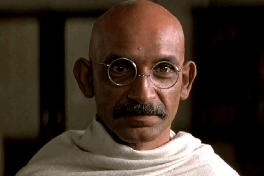 This image shows a bald man with round glasses and a mustache, wearing a simple white robe. His intense and focused expression, combined with the traditional attire, suggests a historical or biographical context.