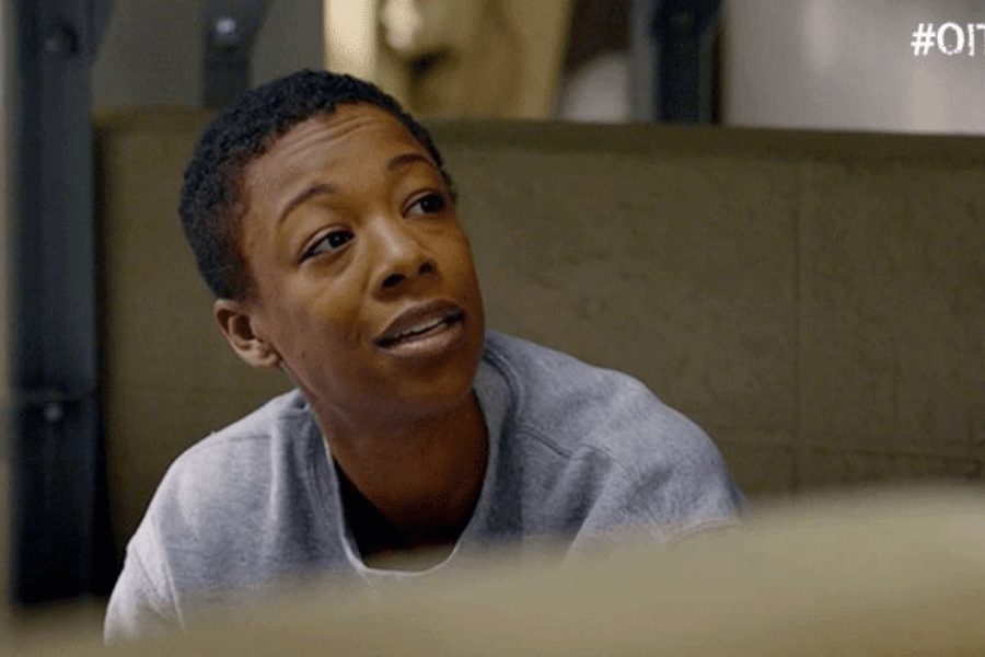 This image shows a woman with short-cropped hair wearing a casual gray sweatshirt, seated in a relaxed indoor setting. She is looking slightly upward with a thoughtful and engaged expression, suggesting she is in conversation. The muted tones of the background add to the intimate, informal atmosphere.