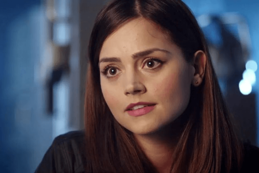 This image shows a young woman with straight brown hair and a thoughtful expression, gazing attentively in a softly lit, indoor setting. Her makeup is subtle, emphasizing her large, expressive eyes. The blurred blue-toned background adds a calm and contemplative atmosphere to the scene.