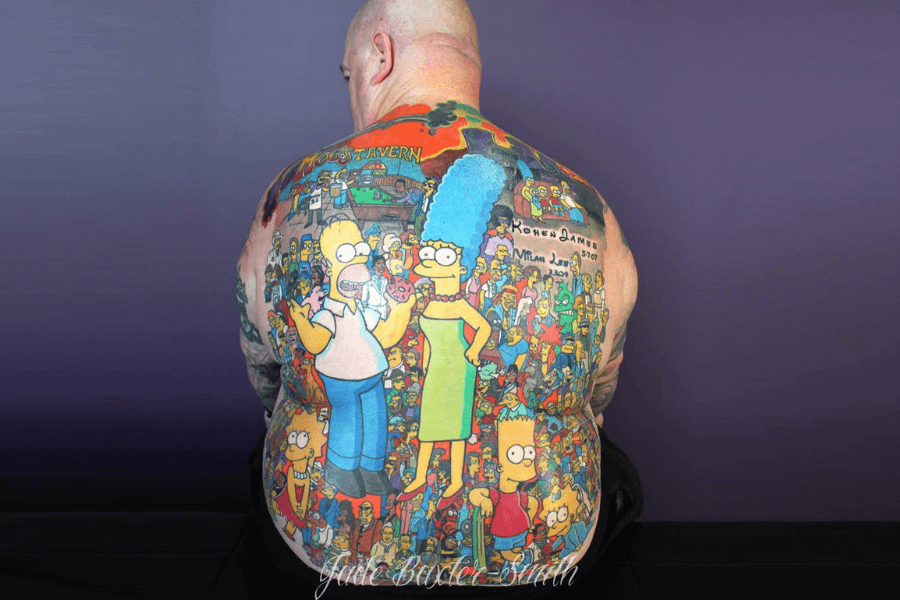 The image shows a man with an extensive back tattoo depicting characters from *The Simpsons*. The tattoo features prominent characters like Homer, Marge, and Bart in the foreground, with a detailed background showcasing Moe's Tavern and a crowd of other characters from the show. The artwork is vibrant and colorful, showcasing the man's dedication to the iconic animated series.