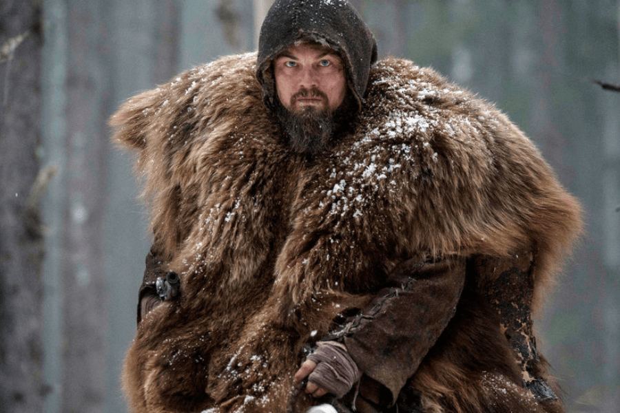 This image features a rugged man in a snowy forest, wearing a large fur cloak and a hood. His intense expression and snow-dusted outfit suggest survival in harsh winter conditions.