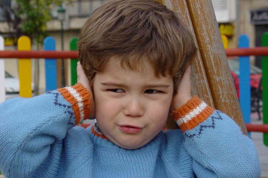 adorable little kid covering his years looking annoyed