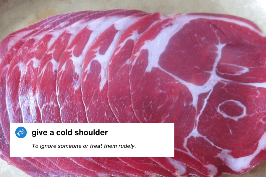  A close-up photograph of thinly sliced raw shoulder meat, with visible marbling and a deep red color. A text overlay in the bottom left corner reads: "Give a cold shoulder – To ignore someone or treat them rudely."