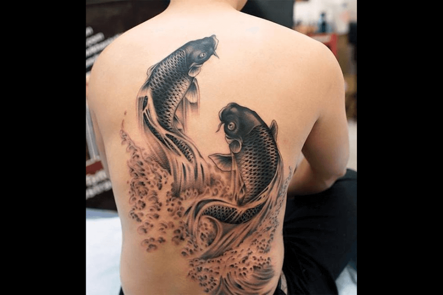 A black and gray tattoo featuring two koi fish swimming amidst swirling water. The fish are detailed with textured scales and flowing fins, creating a dynamic and balanced composition.