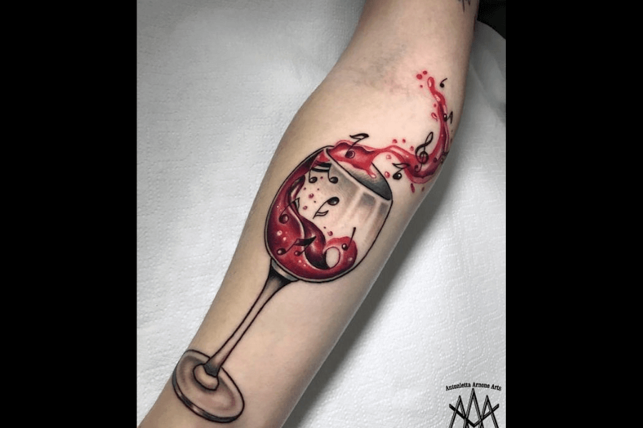 A tattoo of a wine glass with vibrant red wine splashing out. The splash forms musical notes in mid-air, blending elements of music and fine wine in a dynamic design.