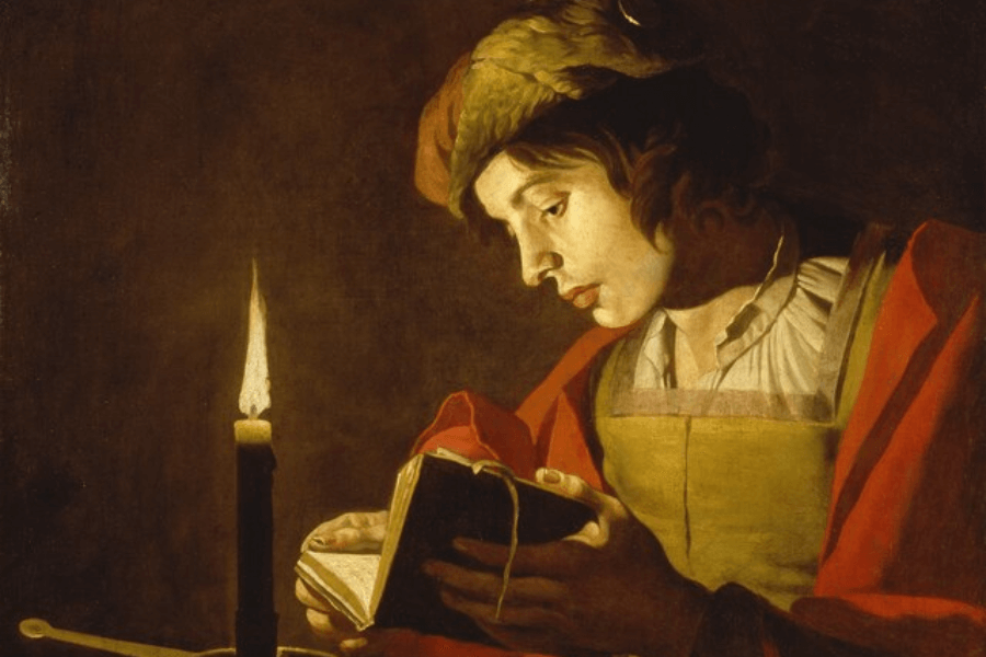 A Baroque-style painting depicting a young man dressed in a red and gold garment, reading a small book by the light of a single candle. His face is illuminated by the warm glow, highlighting his concentrated expression. The dramatic contrast between light and shadow, characteristic of chiaroscuro technique, creates an intimate and contemplative atmosphere.