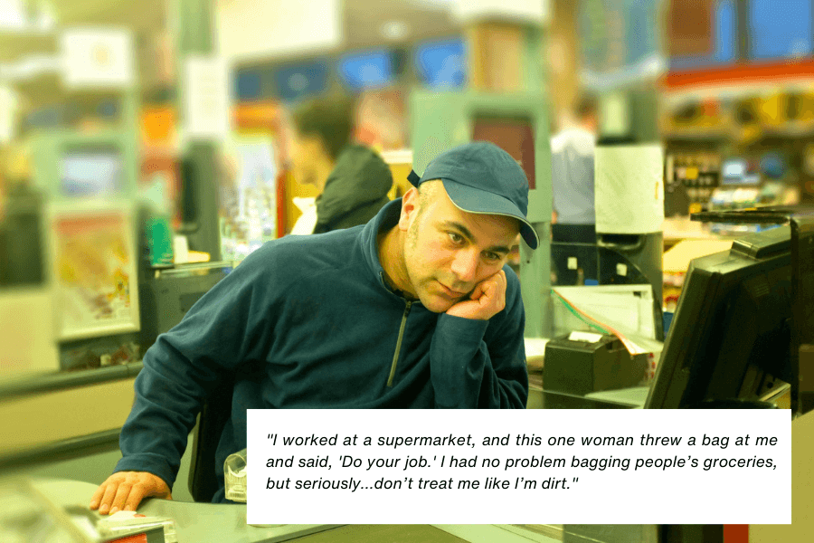 This image shows a supermarket cashier leaning on the counter with a tired or frustrated expression, wearing a blue zip-up sweater and a matching cap. The background is blurred, showing a typical grocery store setting with customers and registers. The quote in the image reads: "I worked at a supermarket, and this one woman threw a bag at me and said, ‘Do your job.’ I had no problem bagging people’s groceries, but seriously... don’t treat me like I’m dirt."