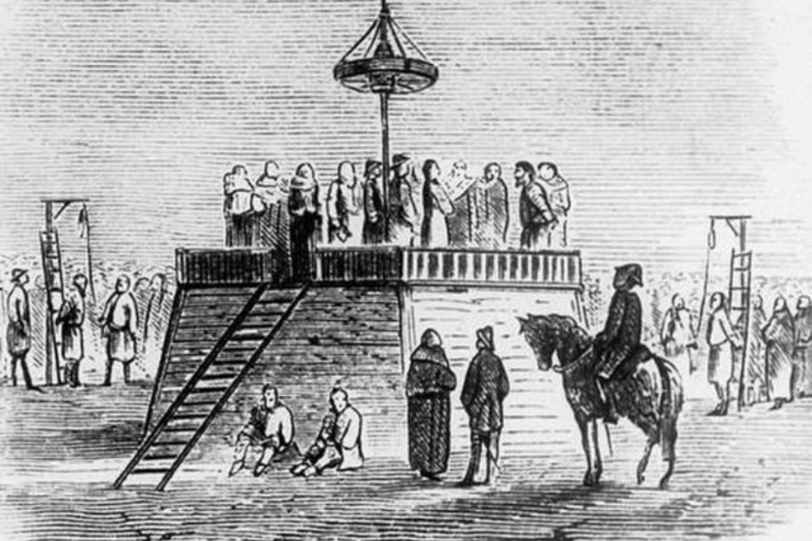 A historical black-and-white engraving depicting a public execution scene on a raised wooden platform, possibly from the 18th or 19th century. A group of people, including officials and condemned individuals, stand on the scaffold, while a crowd gathers around. Gallows with hanging ropes are visible in the background, and a soldier on horseback observes the scene. The image captures the solemnity and spectacle of public punishments from a bygone era.