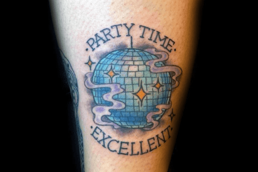 A vibrant tattoo of a blue disco ball with sparkling highlights, surrounded by wispy purple smoke and small star-like accents. The text "Party Time" is inked above the disco ball, and "Excellent" is written below, creating a celebratory and playful vibe. The design is bold and fun, reminiscent of a lively party atmosphere.