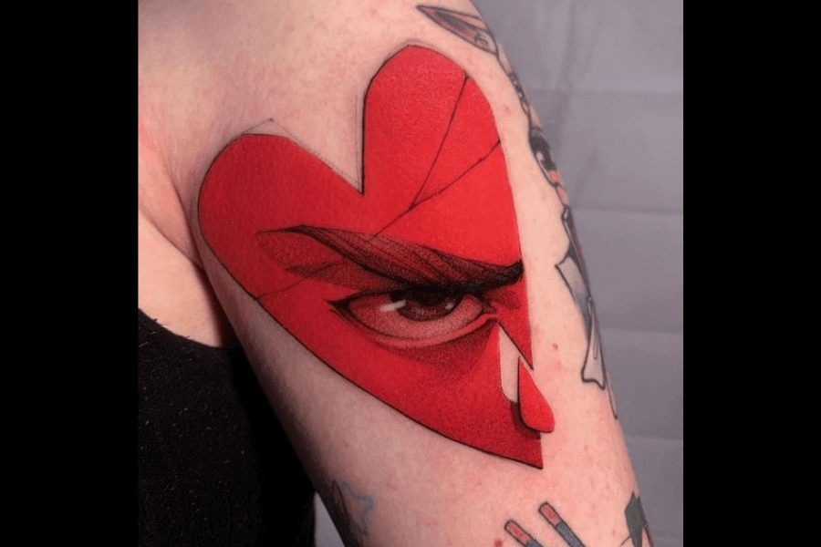 A bold tattoo of a red heart shape that incorporates a sharp, intense eye with detailed shading and defined brows, giving it a dramatic and expressive look. The heart features angular lines that add depth and a stylized artistic touch. This design combines vivid color and intricate detail to create a striking, enigmatic image.