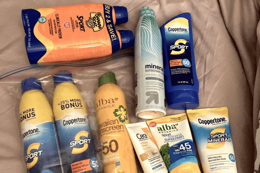 A collection of sunscreen bottles and tubes laid out on a soft surface, featuring various brands such as Banana Boat, Coppertone, Alba Botanica, and CeraVe. The sunscreens include both spray and lotion formulas, with SPF ratings ranging from 30 to 50, designed for sport, mineral protection, and Hawaiian-themed skincare. The assortment suggests a well-prepared traveler ready for a sunny beach or cruise vacation.