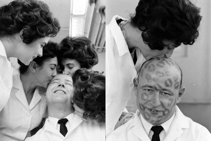 A pair of black-and-white photographs capturing a lighthearted moment in a mid-20th-century setting. In the left image, a bald man in a white coat and tie is surrounded by several women in similar attire, all playfully kissing his head as he smiles with his eyes closed. In the right image, the same man is shown with numerous lipstick marks covering his bald scalp while a woman plants one final kiss on top. His amused expression and the playful nature of the scene suggest a fun office or medical workplace prank.