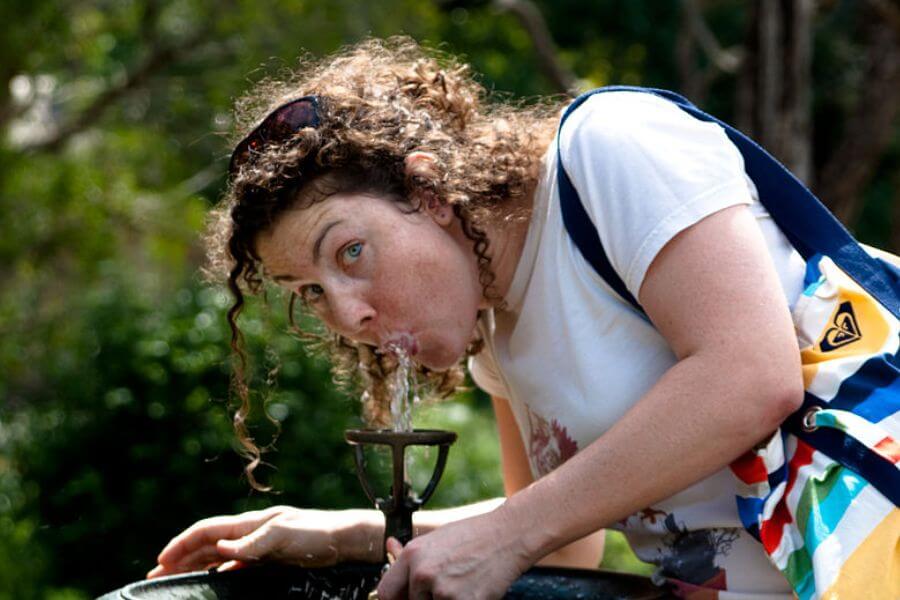 woman drinking water from a water fountain at a park