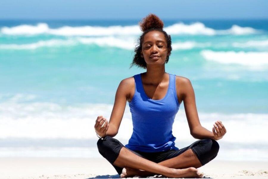 Young black woman smiling while meditating at the beach