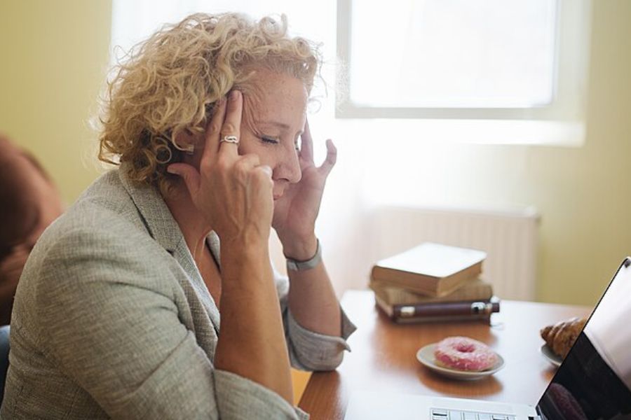 Stressed woman sitting at her office table and pressing the temples on her head with her fingers.
