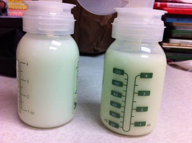  Two plastic baby bottles filled with freshly pumped breast milk sit on a countertop. The bottles have green measurement markings in milliliters and ounces, with screw-on lids and pump attachments on top.