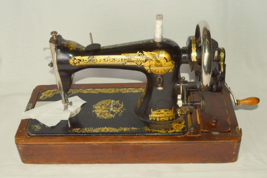 The photograph shows a vintage Singer sewing machine, adorned with intricate gold detailing. Its black cast-iron body sits atop a wooden base, exuding an air of craftsmanship and durability. A hand-crank with a wooden handle suggests a time before electricity ruled the world of stitching. This elegant relic was once a household essential, transforming fabric with each meticulous turn of the wheel.