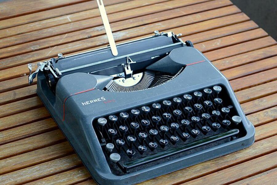 The photograph shows a vintage Hermes Baby typewriter resting on a wooden table. Its sleek black keys and matte gray body give it a classic, utilitarian charm. A metal carriage return lever stands upright, ready for the next line of prose or poetry. This compact and portable machine once empowered writers with the rhythmic clack of inspiration.