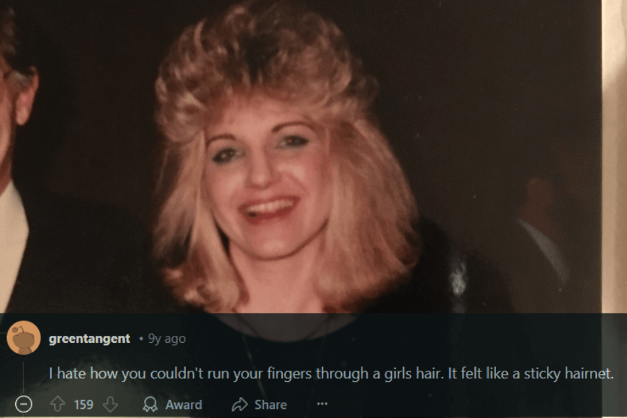 A smiling woman with voluminous, feathered blonde hair, styled in the quintessential 1980s fashion with lots of height and layers. She is wearing a dark outfit, and her blue eyeshadow adds to the signature look of the era. A comment below humorously complains about how heavily styled hair from that time felt "like a sticky hairnet."