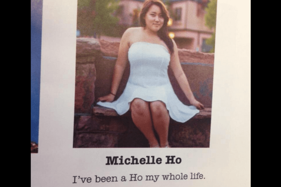 A high school yearbook photo of Michelle Ho, a young woman wearing a strapless white dress, sitting on a stone ledge with a relaxed pose. The background features a warm outdoor setting with buildings and greenery. Below her name, her humorous yearbook quote reads, "I’ve been a Ho my whole life," making a playful reference to her last name.